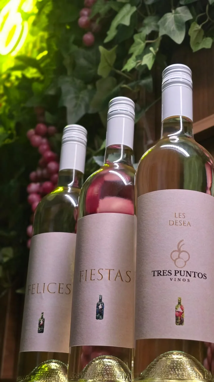 Tres botellas con etiquetas rosadas que juntas dicen Felices Fiestas Les Desea Tres Puntos Vinos